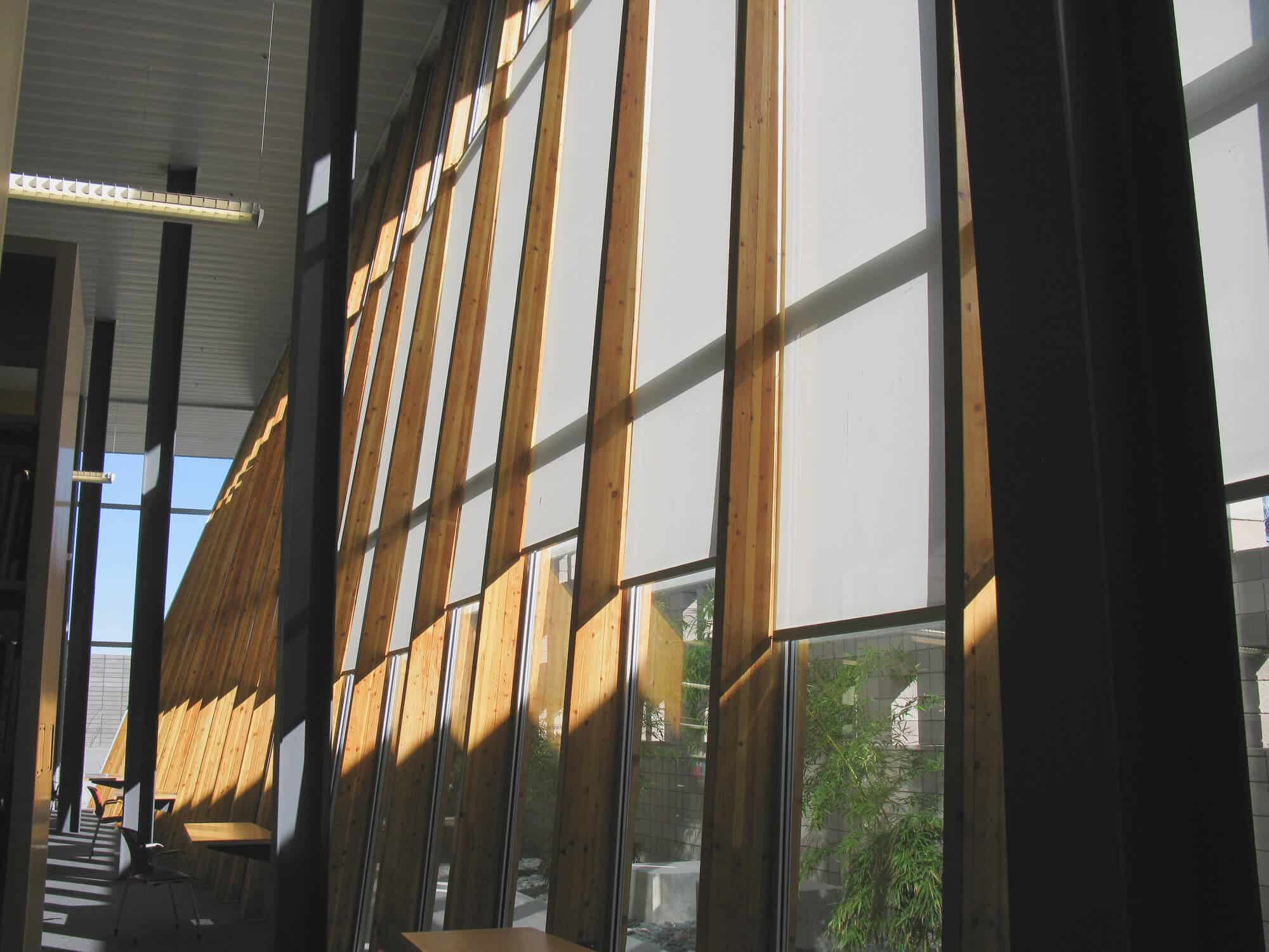 Modern building interior with tall wooden beams and large windows with automated blinds.