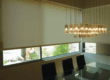 White window shades covering most of a dining room behind the dining room table.