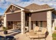 Grey and brown brick home with solar shades covering the outdoor patio against the bright sun.