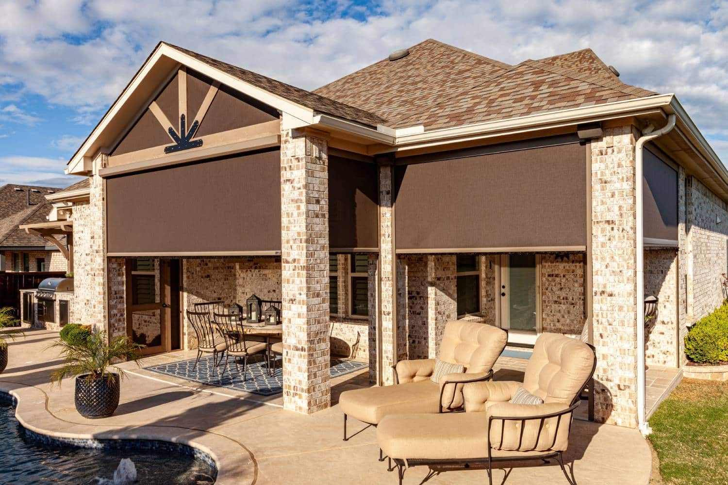 Grey and brown brick home with solar shades covering the outdoor patio against the bright sun.