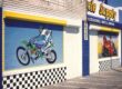 Customized rolling shutters for a Bicycle Supply store. Images of people on motor bikes are painted over the shutters in various colors.